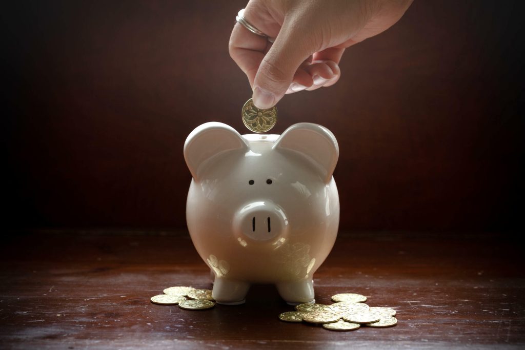 A piggy bank stands in dramatic lighting with gold coins around its feet.