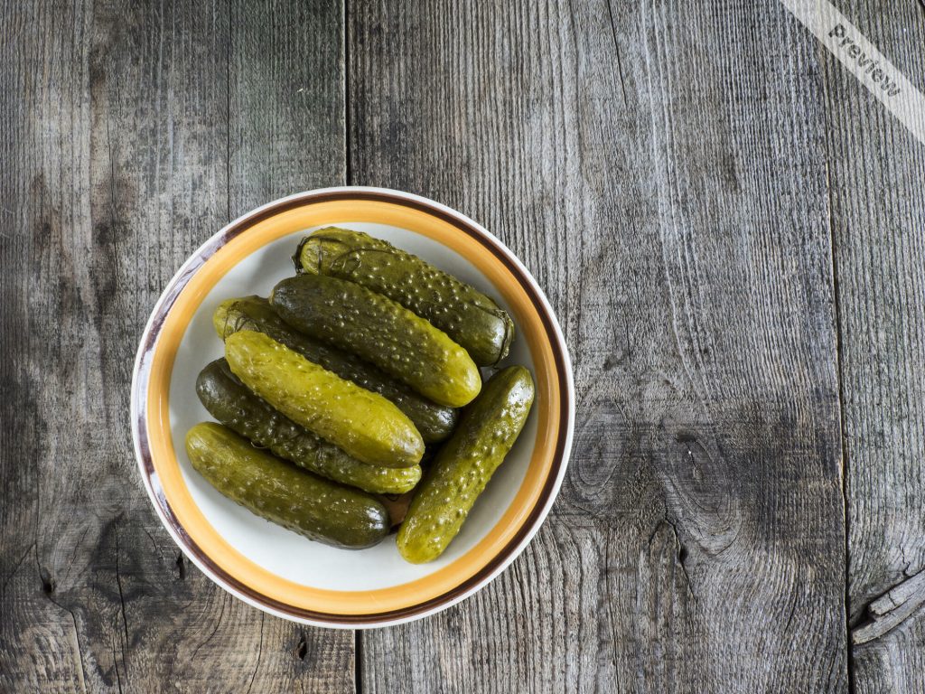 Pickled green gherkins in a bowl on weathering wooden background