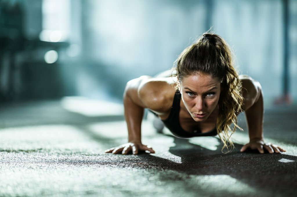 Young female athlete exercising push-ups within a gym and looking at the camera.
